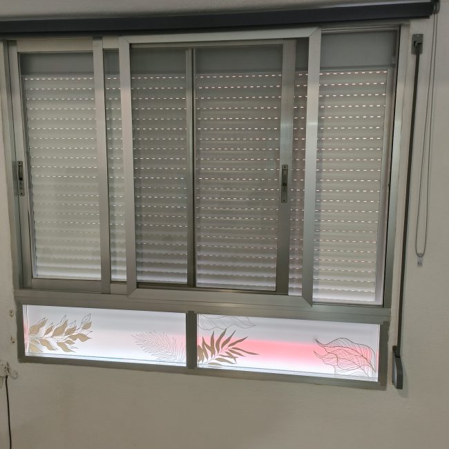 Ventana con marco de aluminio con dos hojas, una mosquitera y una persiana, con unos marcos de cristal en la parte inferior